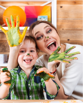 a women and a boy smiling at the camera with green pain on their hands from finger painting