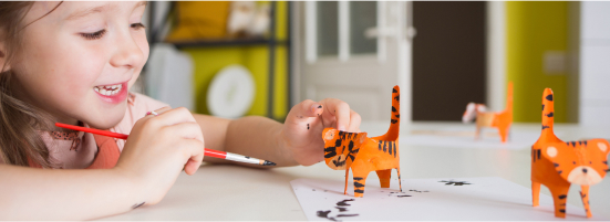 girl doing crafts painting to small paper made orange cats