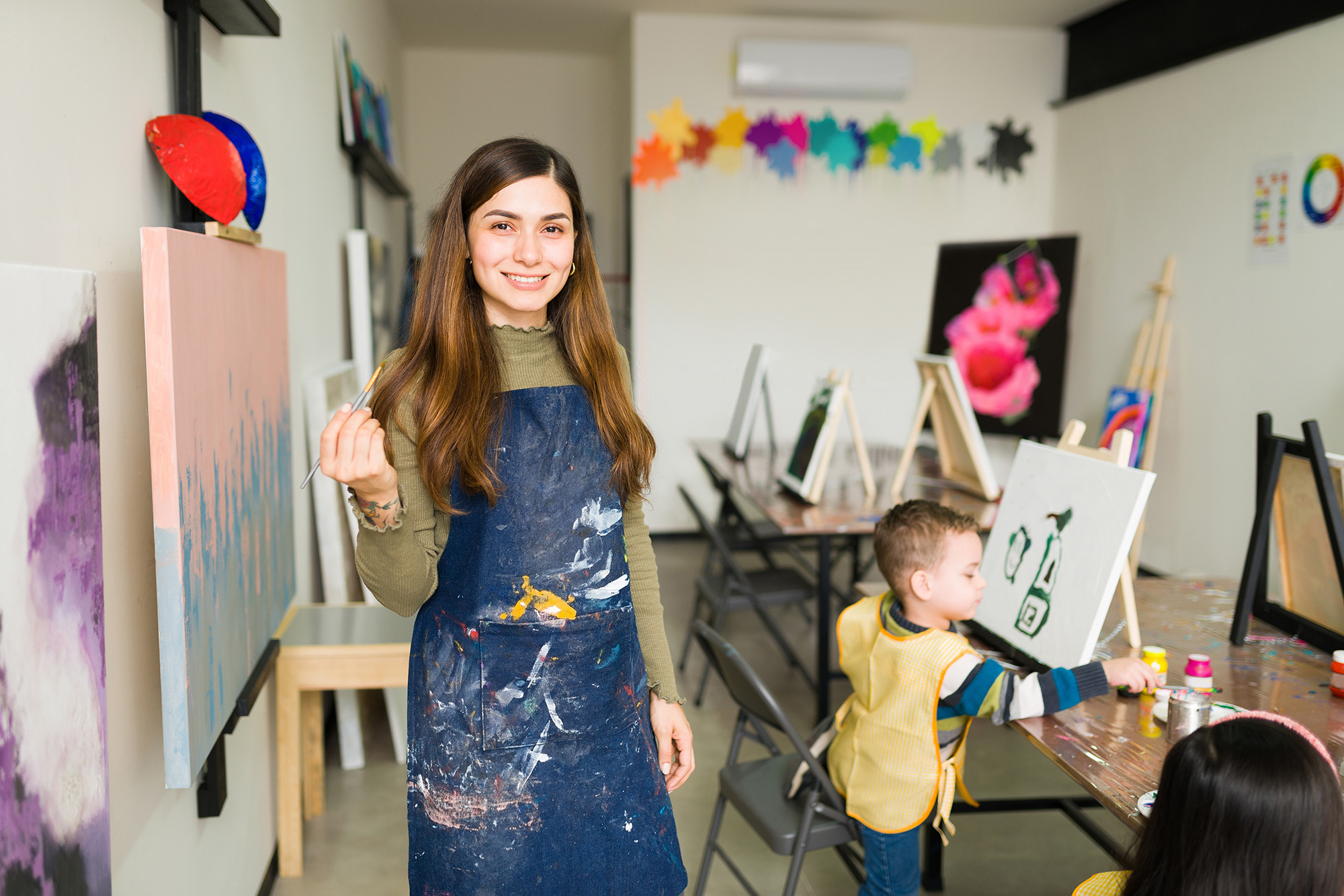art teacher smiling at the camera with arts and crafts in the background