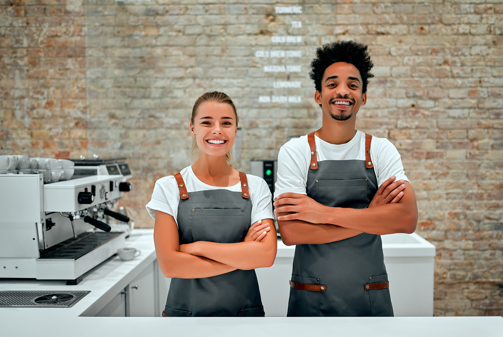 two cafe workers standing next to each other with their arms crossed while smiling